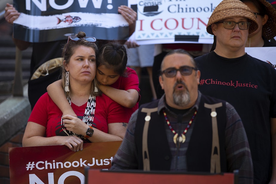 caption: Chinook Indian Nation councilwoman Rachel Cushman listens with her son, Kanim Cushman-White Eyes, 9, as Chinook Indian Nation tribal members and allies gathered on the steps of the Henry M. Jackson Federal building to rally for the restoration of federal recognition on Monday, August 29, 2022, in Seattle. 