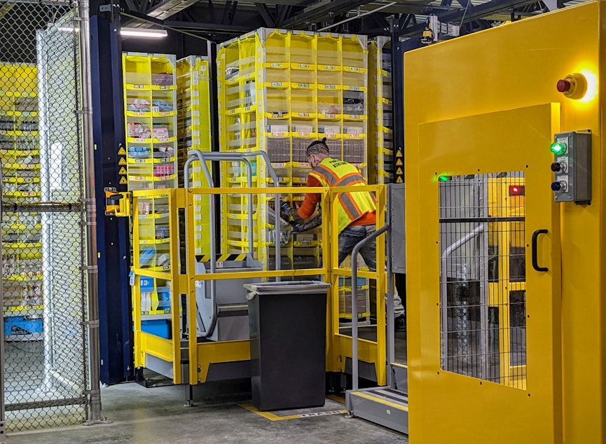 caption: A picker loads items onto a shelf that then gets ferried around the warehouse on a robotic dolly.