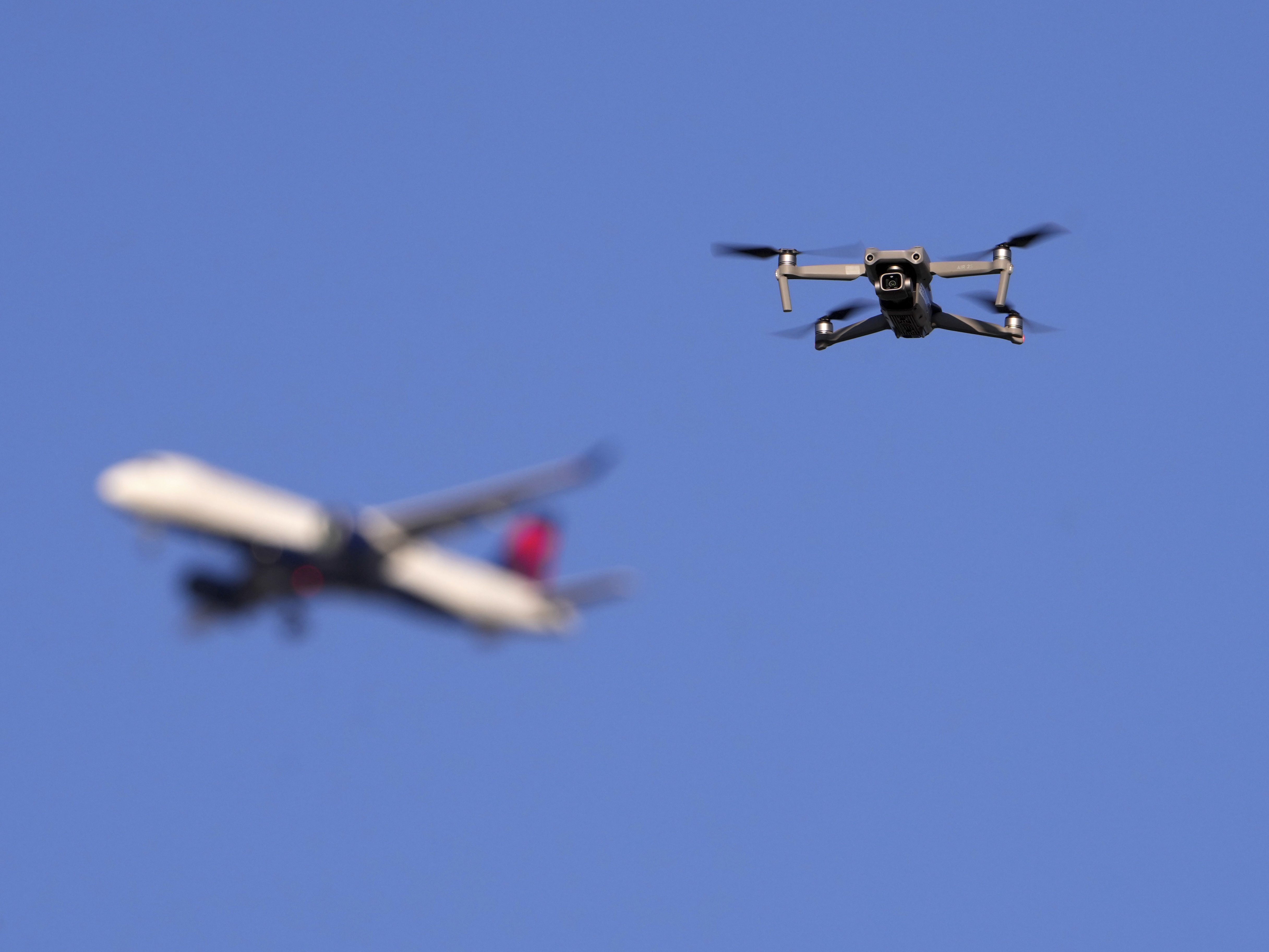 caption: A drone hovers in airspace outside the safety perimeter surrounding St. Louis Lambert International Airport as an airliner approaches for a landing on March 10.