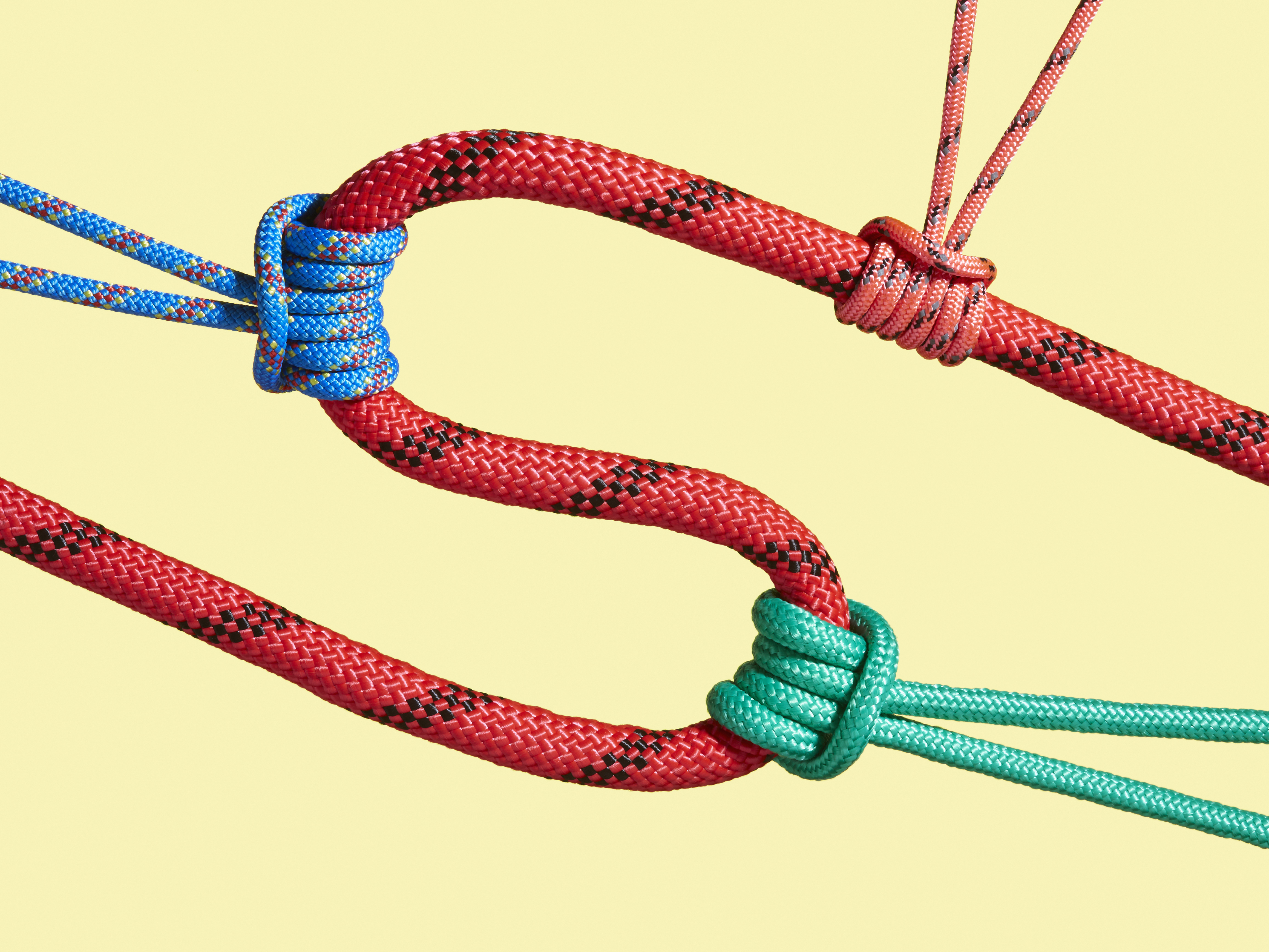 caption: Red S-shaped rope being tugged by three different knots. Each knot is a different color — blue, orange, and green. Yellow background.