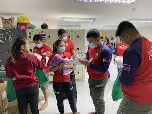 caption: Staffers distribute the required personal protective gear before they transfer a COVID-positive patient to a hospital. They'll wear a gown, gloves, mask and face shield.