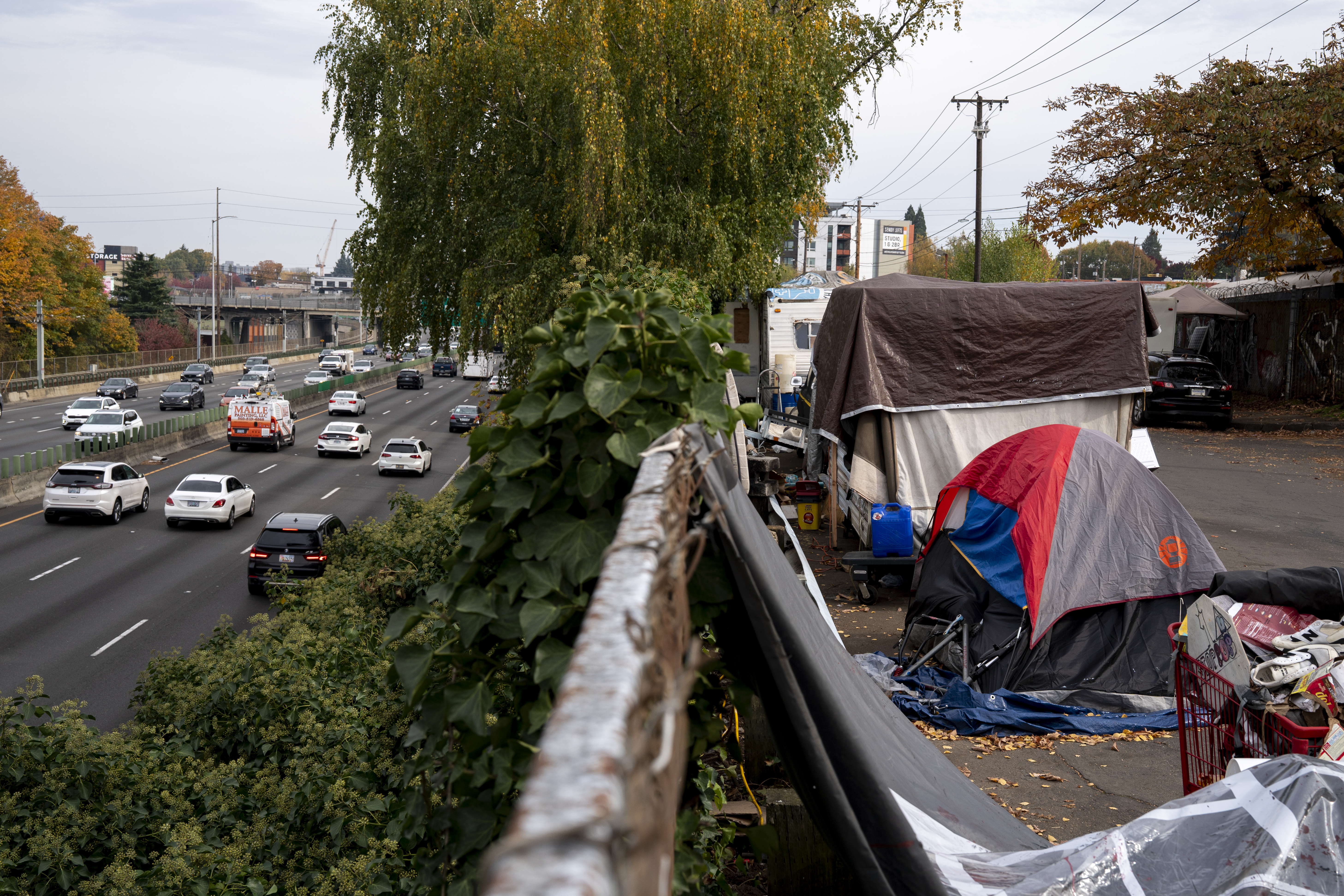 caption: RVs and tents line a street above the highway at an encampment of unhoused people in Portland, Oregon, on Oct. 31, 2025.
