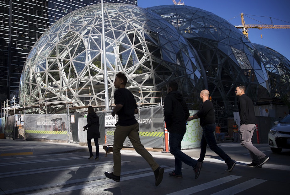 caption: A group of people jog across Lenora Street in front of Amazon's biodomes, in Seattle.