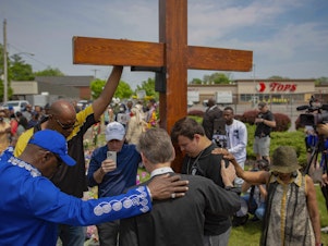 caption: A new civil lawsuit filed Wednesday by families of the Buffalo Tops mass shooting victims targets a number of social media companies, gun retailers, a body armor manufacturer and the mass shooter's parents. Here, a group prays at the site of a memorial for the victims of the Buffalo supermarket shooting outside the Tops Friendly Market on Saturday, May 21, 2022, in Buffalo, N.Y.