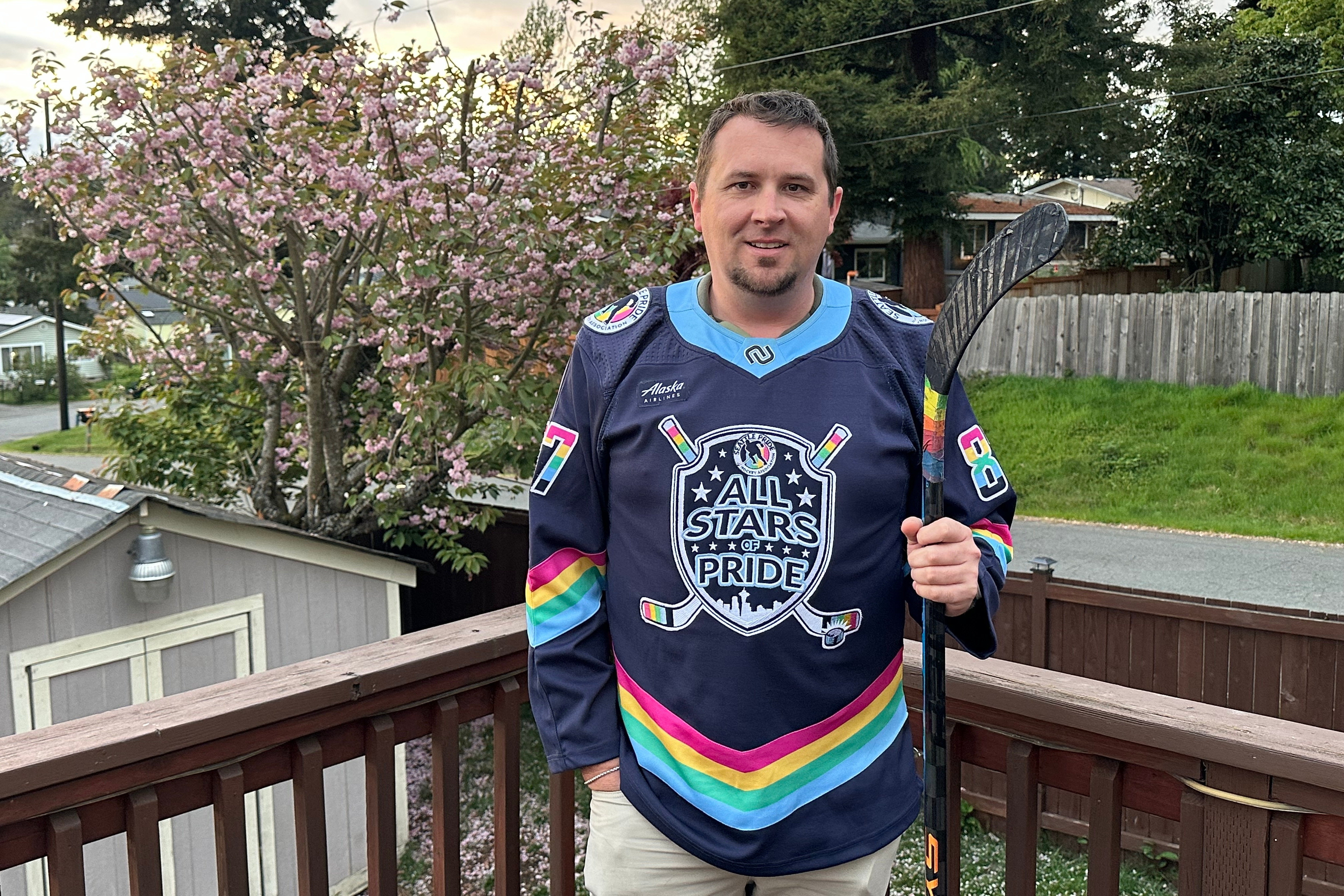 caption: Steven Thompson, co-founder of the Seattle Pride Hockey Association (SPHA), poses for a photo with his stick that features pride tape and a SPHA sweater at his home in Des Moines, Wash., Monday, April 27, 2026. 