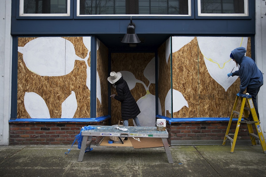 caption: Dawna Holloway, left, and Sallyann Corn paint lemons onto the boarded up facade of fruitsuper, a retail shop and wine bar, on Thursday, March 26, 2020, on First Avenue South in Seattle. "Just to bring a little joy to the neighborhood," said Corn. "We could all use more of that."