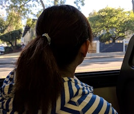 caption: The author's mother, Jenny Huang, looks out of a bus window. In August 2016, she was slapped by a white woman for having her purse on the seat next to her on the bus as she napped.