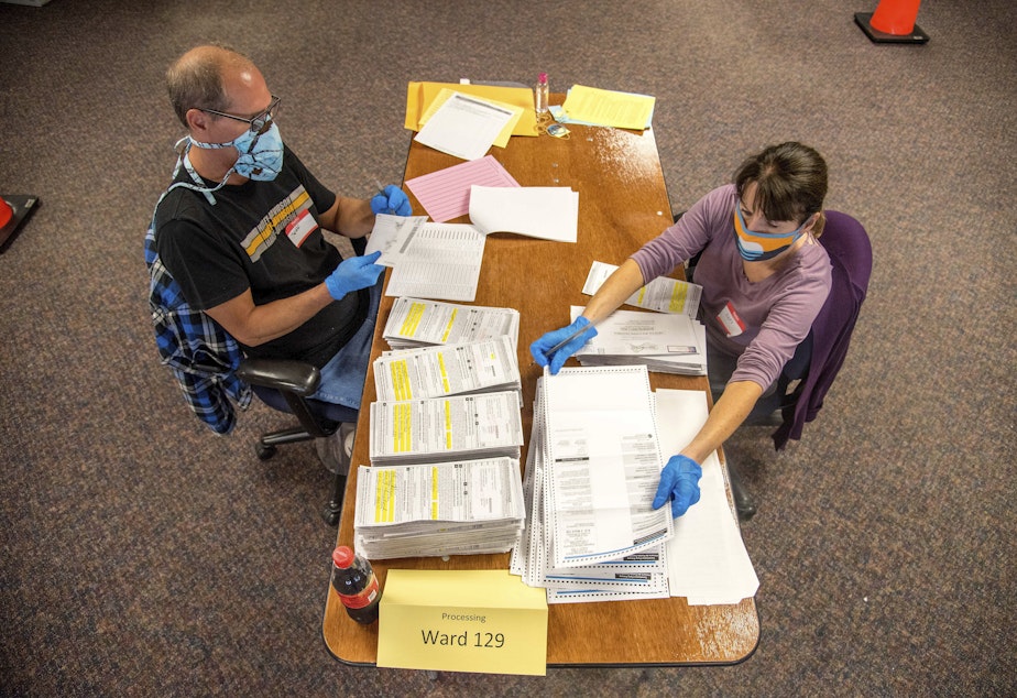 caption: In this photo provided by Wisconsin Watch, election workers Jeff and Lori Lutzka, right, process absentee ballots at Milwaukee's central count facility on Aug. 11, 2020. (Will Cioci/Wisconsin Watch via AP)