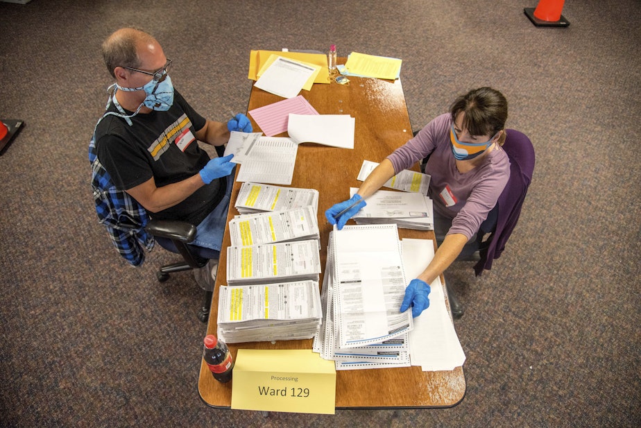 caption: In this photo provided by Wisconsin Watch, election workers Jeff and Lori Lutzka, right, process absentee ballots at Milwaukee's central count facility on Aug. 11, 2020. (Will Cioci/Wisconsin Watch via AP)