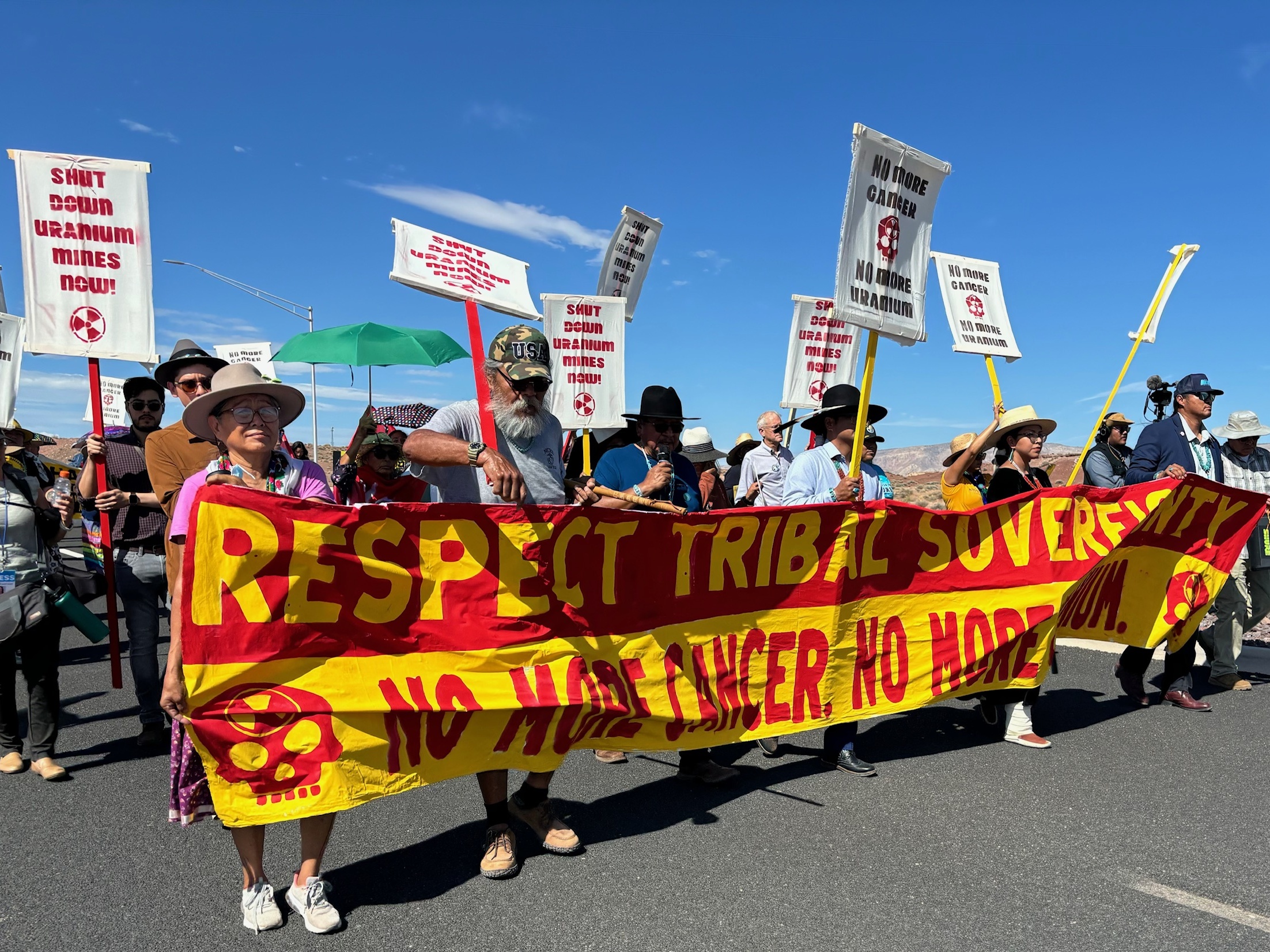 caption: Protestors, led by Navajo Nation President Buu Nygren, marched along Highway 89 in Cameron on Aug. 2, 2024 to protest uranium hauling through the reservation. The highway was part of the route taken by trucks from the Pinyon Plain Mine near the South Rim of the Grand Canyon three days earlier when they began uranium ore transportation through a large swath of the nation.