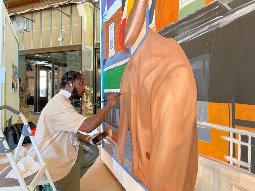 caption: Al-Baseer Holly working on a  painting titled "From the Bottom," which appears in the Forest for the Trees art exhibit. 