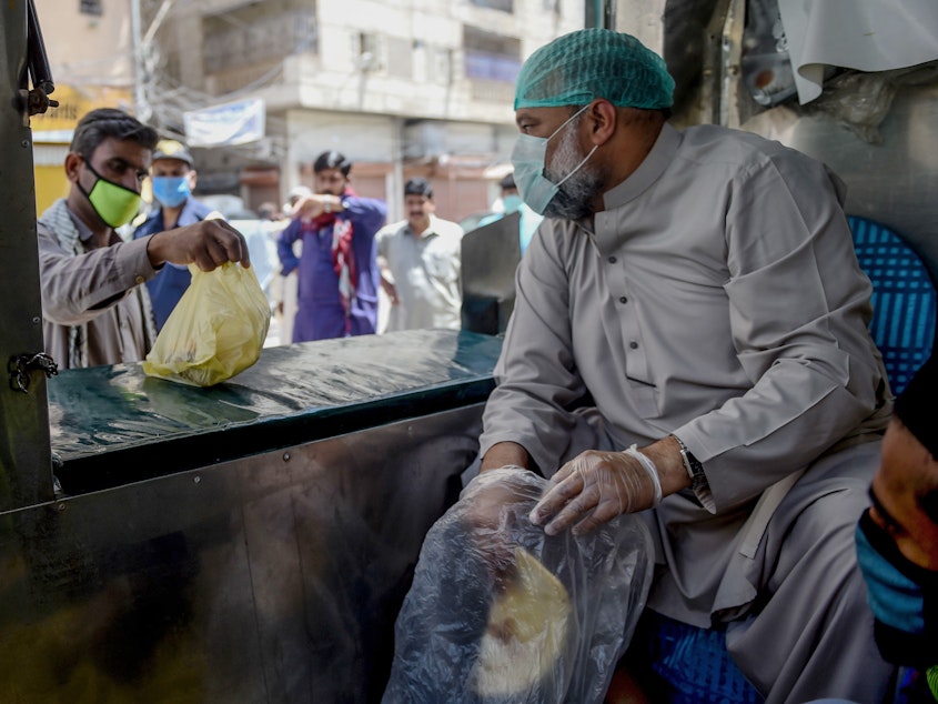 caption: A municipal worker in Karachi hands out bags of food — part of government efforts to help those who've lost their livelihood during Pakistan's lockdown to stem the spread of the coronavirus.