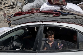 caption: A young boy looks out from a car as members of a Palestinian family leave Rafah in the southern Gaza Strip with personal belongings on March 31.