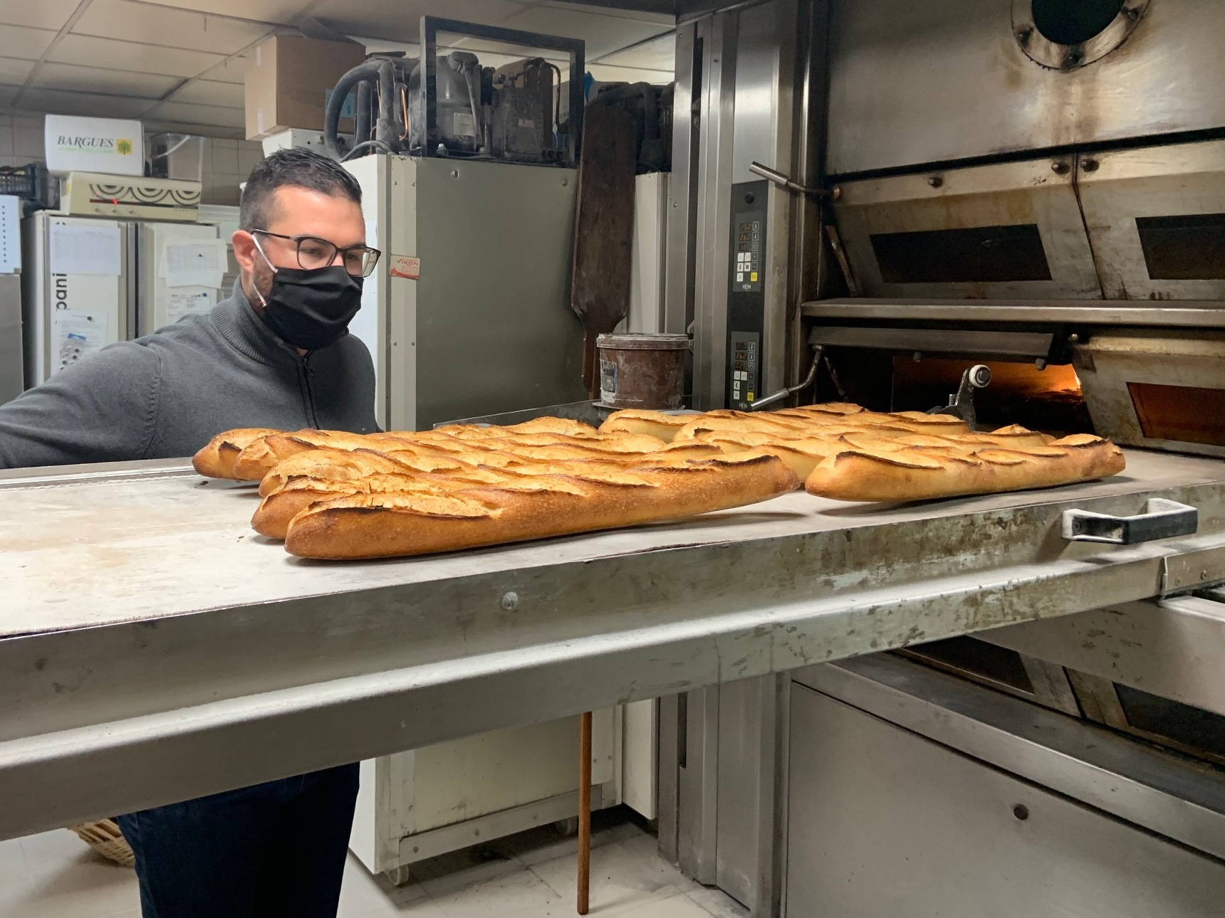 caption: Tony Doré wears a face mask as baguettes cool in his bakery in Paris' 15th arrondissement.