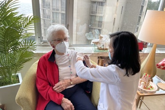 caption: Flor Craig (r) injects Parkshore resident Lovie Therriault with her first dose of the Pfizer-BioNTech Covid vaccine, December 21, 2020. 