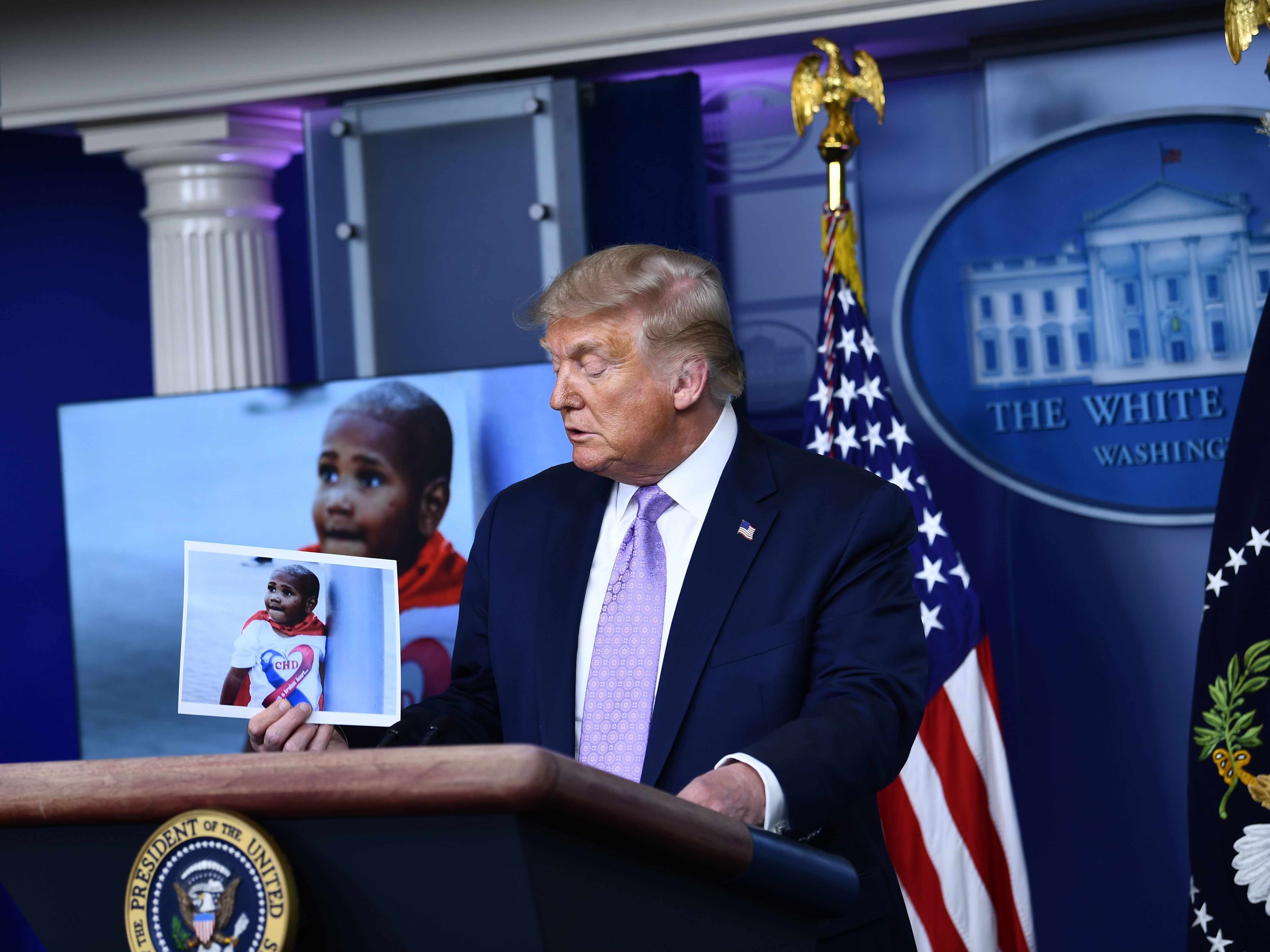 caption: President Trump holds a photo of LeGend Taliferro, a boy killed in Kansas City, during a White House news conference.