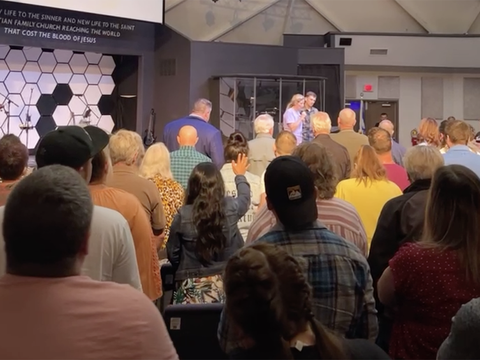 caption: In this screenshot from a Facebook Live video of the church service by Maisey Cook, a woman takes the stage at New Life Christian Church and World Outreach in Warsaw, Ind. with her husband to tell her story of how Pastor John Lowe II had sex with her she was 16 years old.
