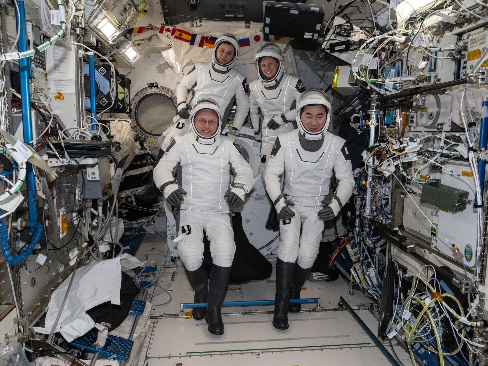 caption: The four SpaceX Crew-11 members gather for a portrait last Friday wearing their pressure suits inside the International Space Station. NASA is returning the crew a month early because one has an undisclosed medical condition. Clockwise from bottom left are, NASA astronaut Mike Fincke, Russian cosmonaut Oleg Platonov, NASA astronaut Zena Cardman, and Japan Aerospace Exploration Agency astronaut Kimiya Yui.