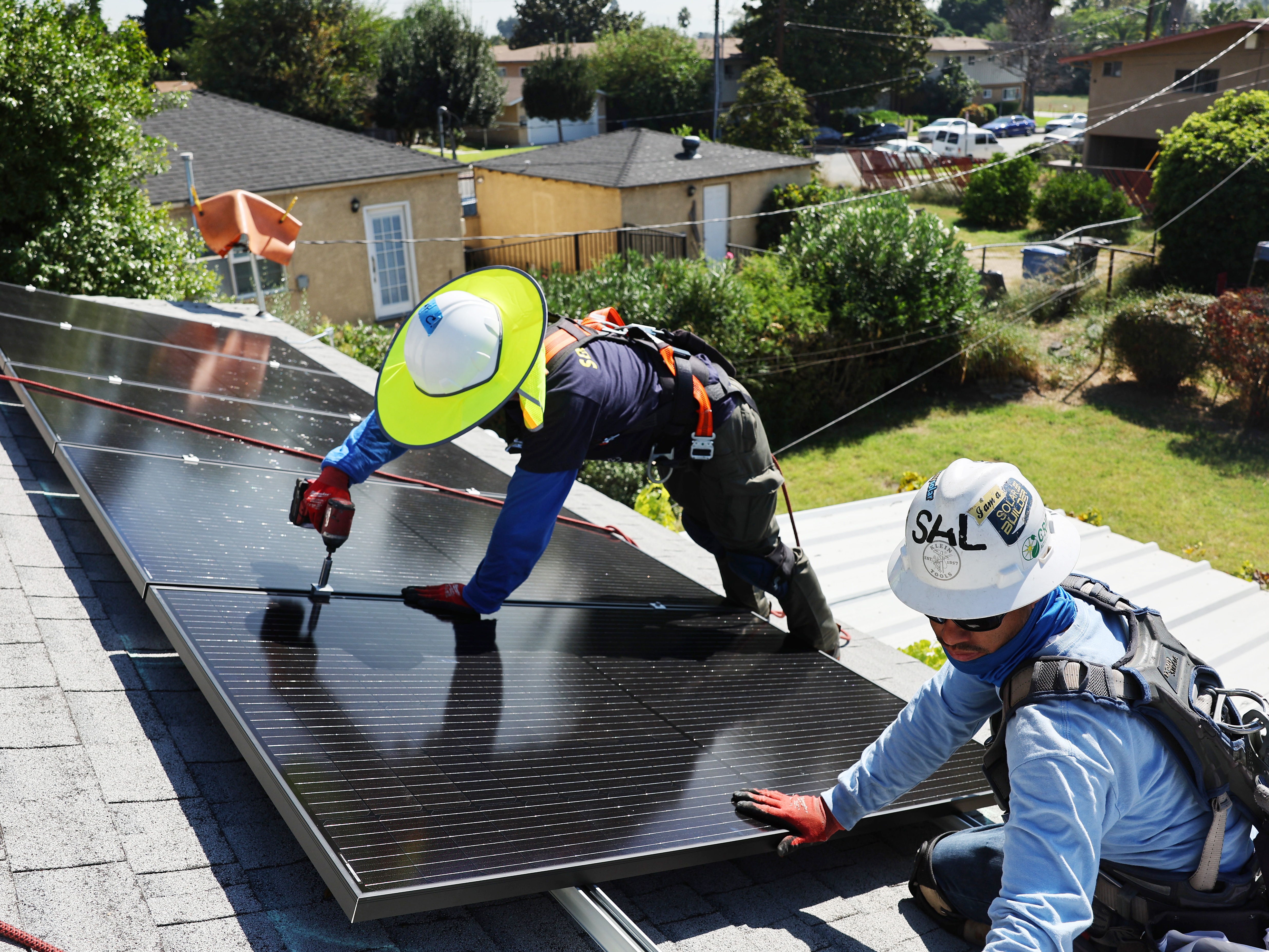 caption: GRID Alternatives employees install no-cost solar panels on the rooftop of a low-income household on October 19, 2023 in Pomona, California.