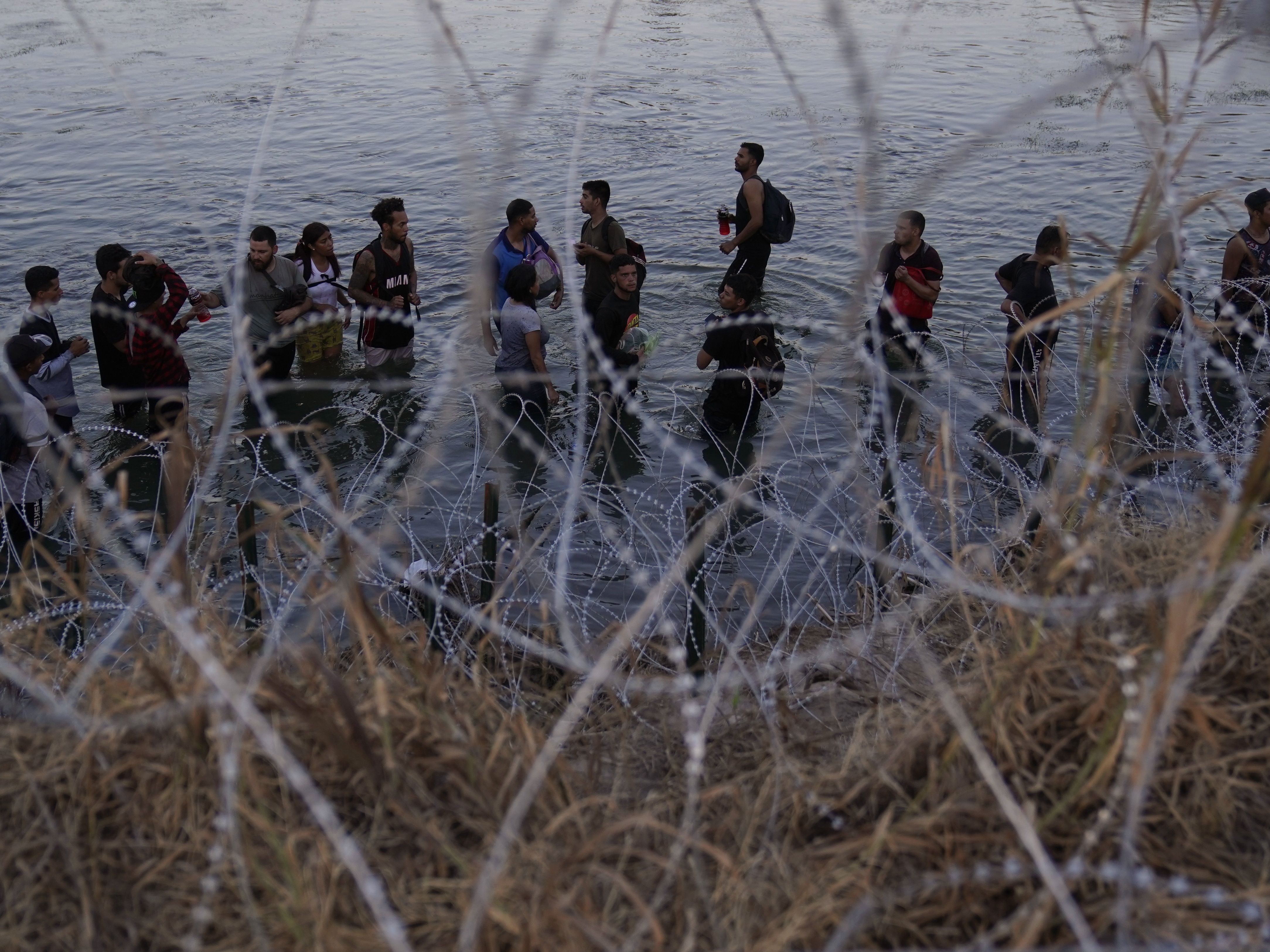 caption: Migrants wait to climb over concertina wire after they crossed the Rio Grande and entered the U.S. from Mexico, Sept. 23, 2023, in Eagle Pass, Texas.