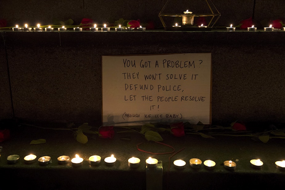 caption: A sign surrounded by lit candles is shown on Monday, October 26, 2020, during the 150th day of protests for racial justice in Seattle at Westlake Park.