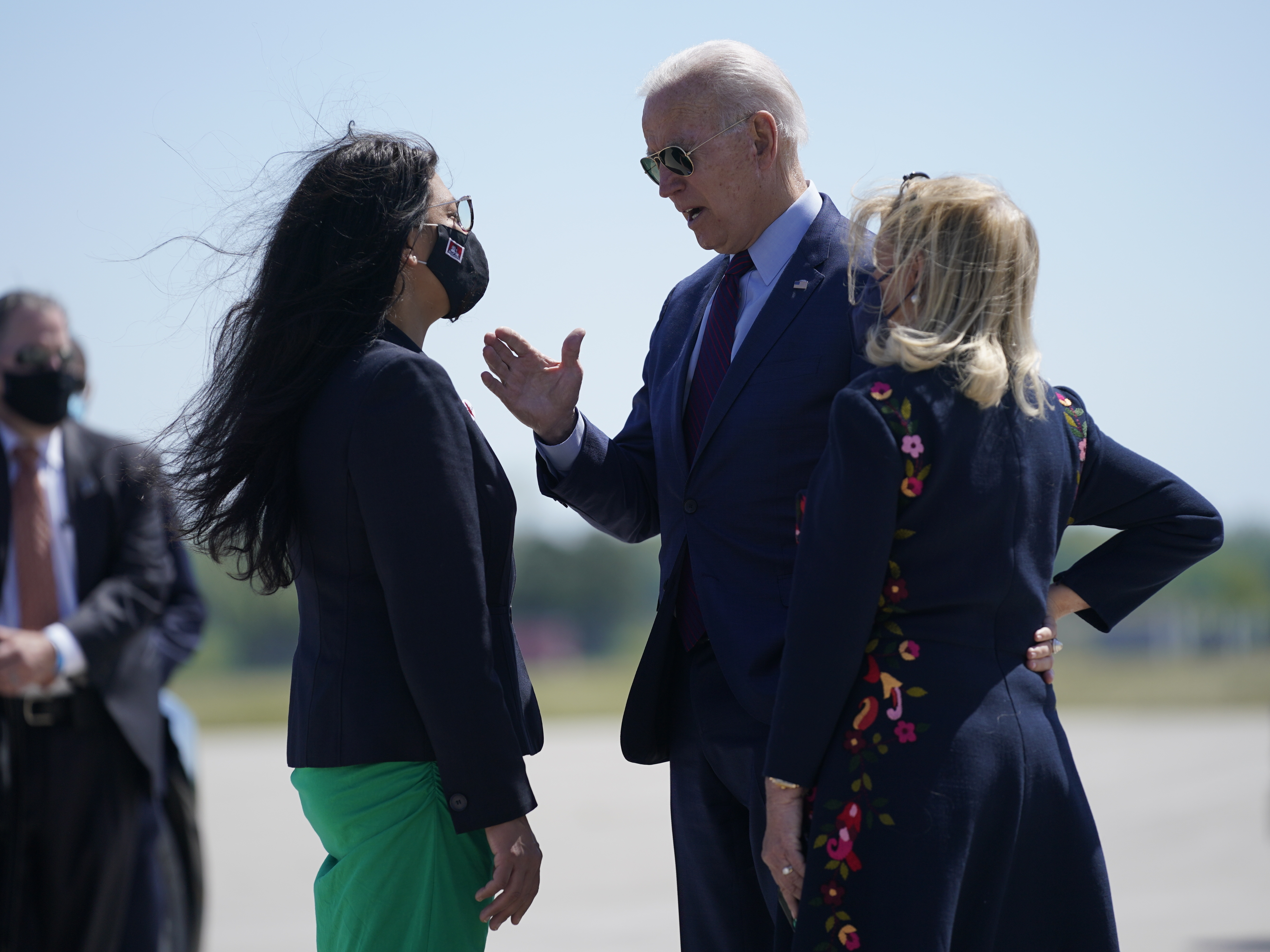 caption: President Biden speaks with Rep. Rashida Tlaib, D-Mich., left, and Rep. Debbie Dingell, D-Mich., as he arrives at in Detroit Tuesday.