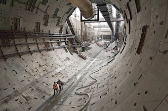 caption: Two workers walk through the first rings of the tunnel toward Bertha, the SR 99 tunneling machine.