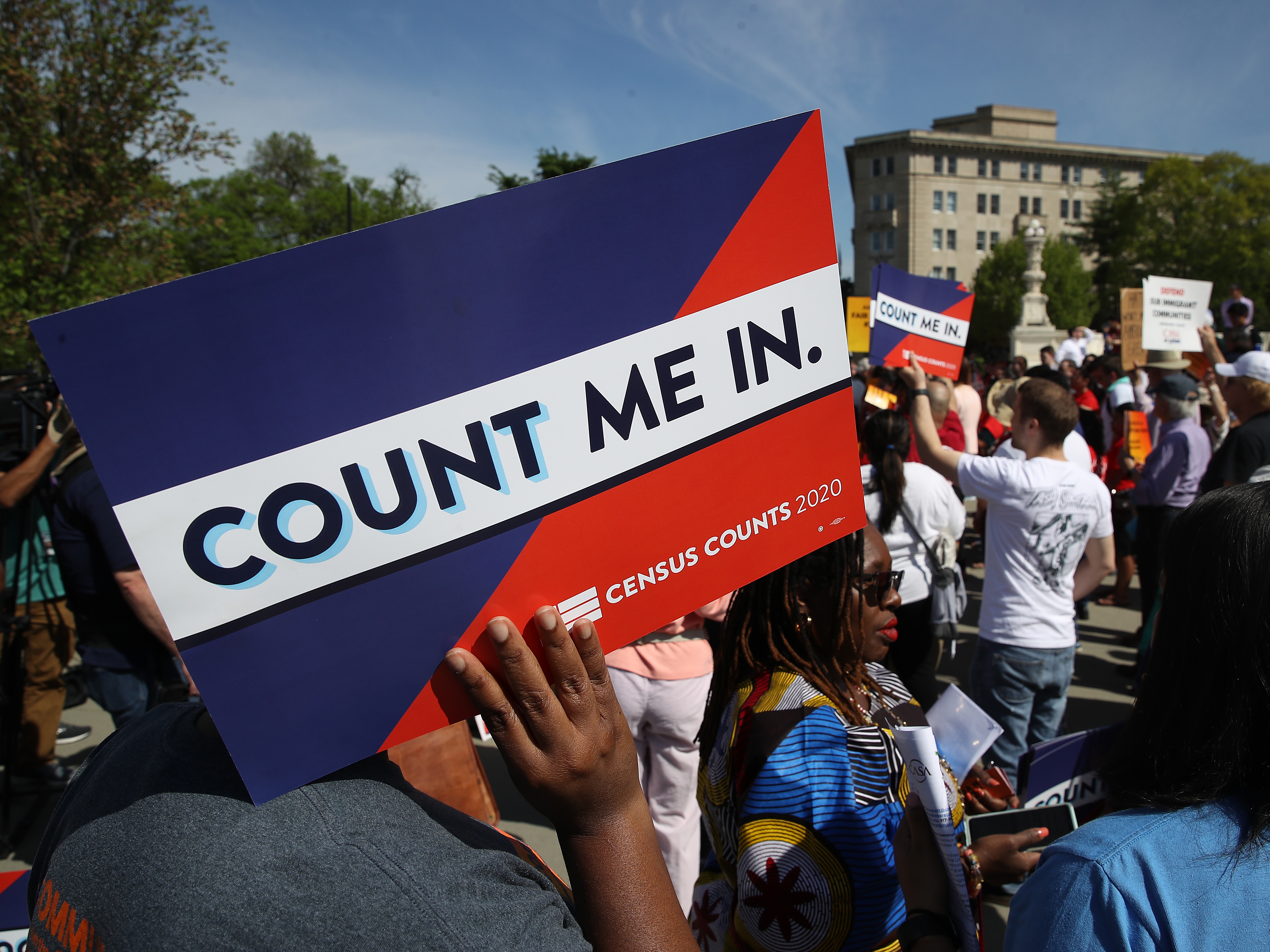 caption: Protesters hold signs saying "COUNT ME IN" at a 2019 rally against the Trump administration's push for a census citizenship question outside the U.S. Supreme Court in Washington, D.C.