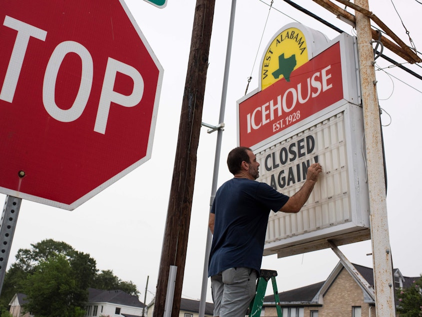 caption: Bar owner Petros J Markantonis changes the marquee outside his bar to "Closed Again" at the West Alabama Ice House in Houston.