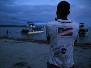 caption: A Venezuelan migrant watches the boat he hopes to take across the Gulf of Urabá once he gets enough money together for the trip.