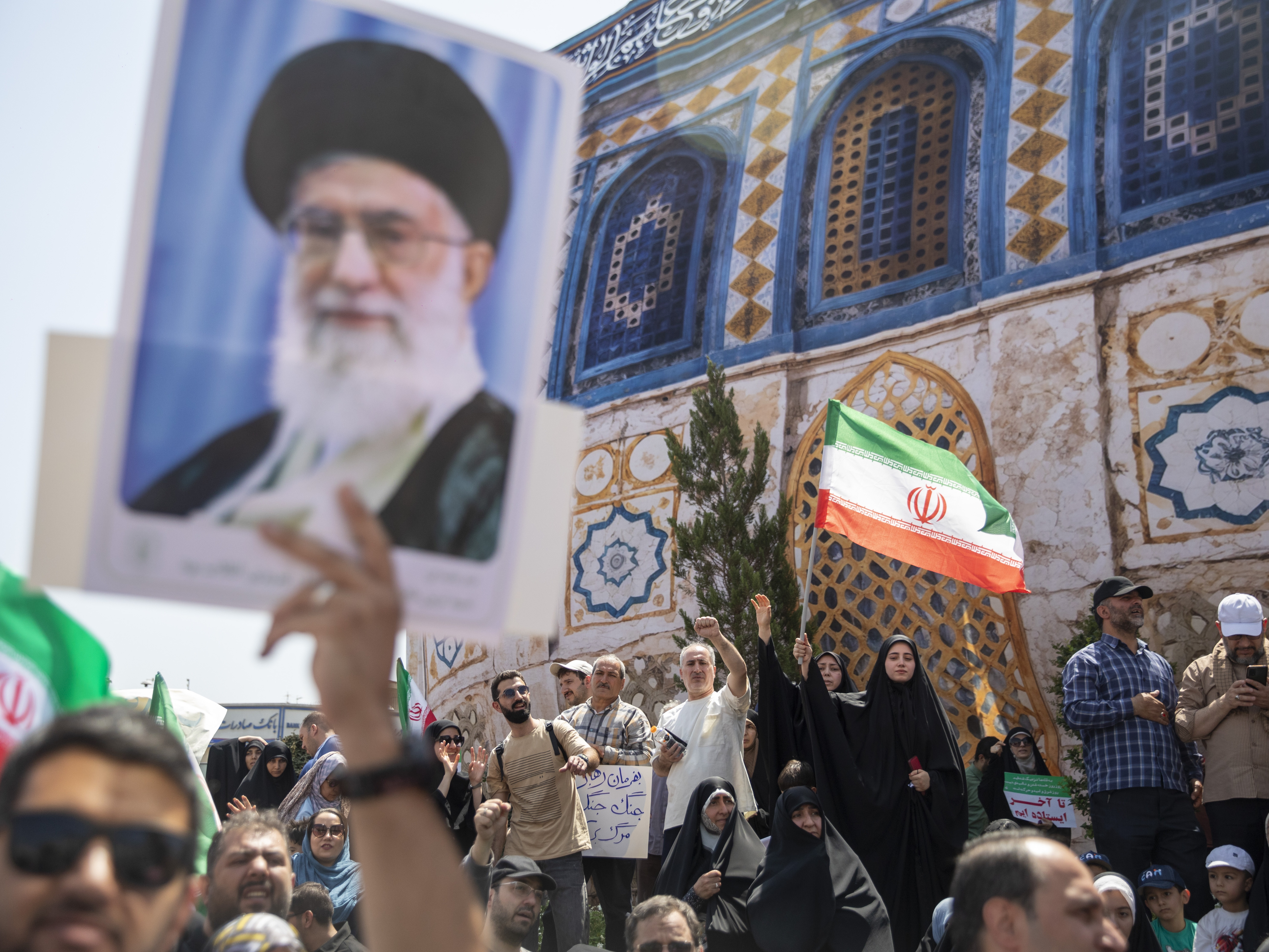 caption: Demonstrators wave Iranian flags as one holds up a poster of Iran's Supreme Leader Ayatollah Ali Khamenei during a protest against Israeli attacks on Iran, after the Friday prayer ceremonies on June 20, 2025 in central Tehran, Iran.