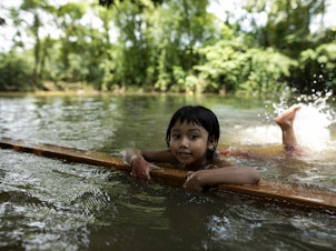 caption: A child learns to swim in a pond in a rural area of Bangladesh.