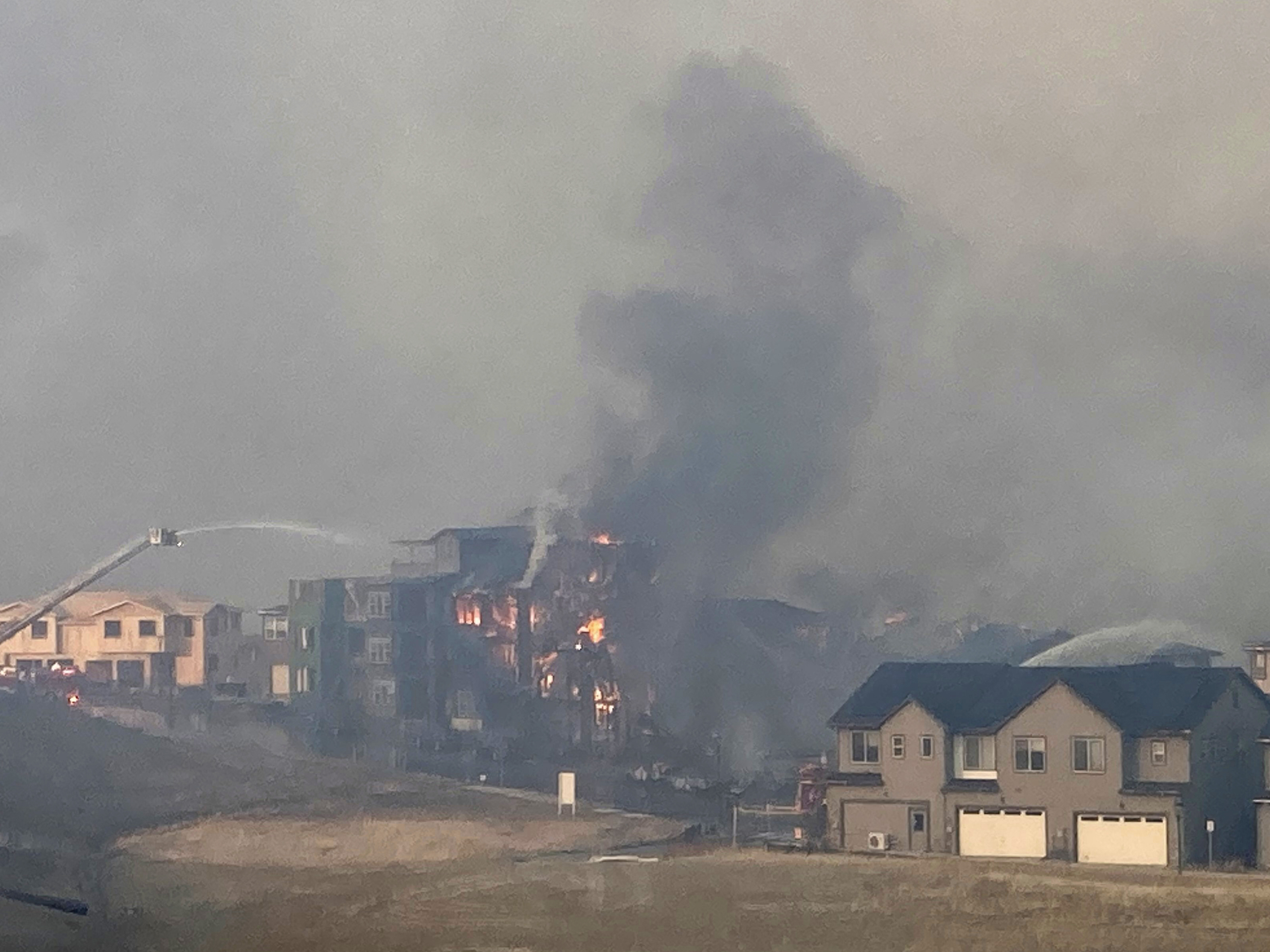 caption: Firefighters spray water on a structure fire as a wildfire burns on Thursday in Superior, Colo.