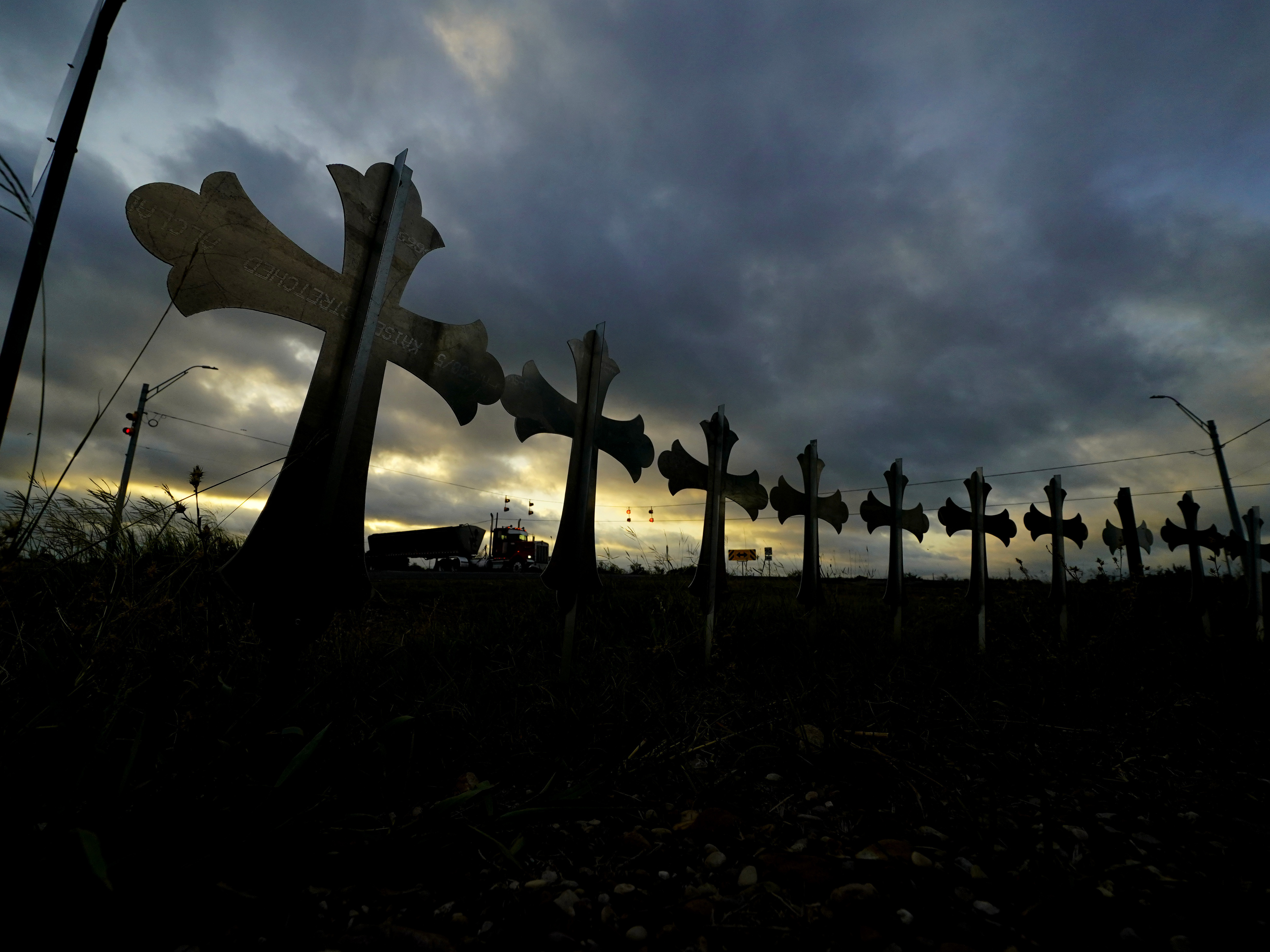 caption: A truck passes crosses placed along the highway to honor the victims killed in the recent school shooting at Robb Elementary School.