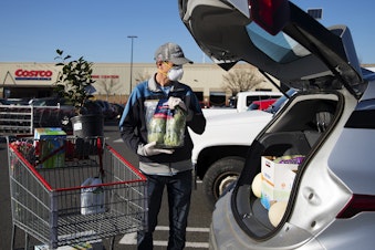 caption: Jon Hartley puts a bag of artichokes into the trunk of his car after shopping at Costco on Wednesday, March 18, 2020, in Seattle. 
