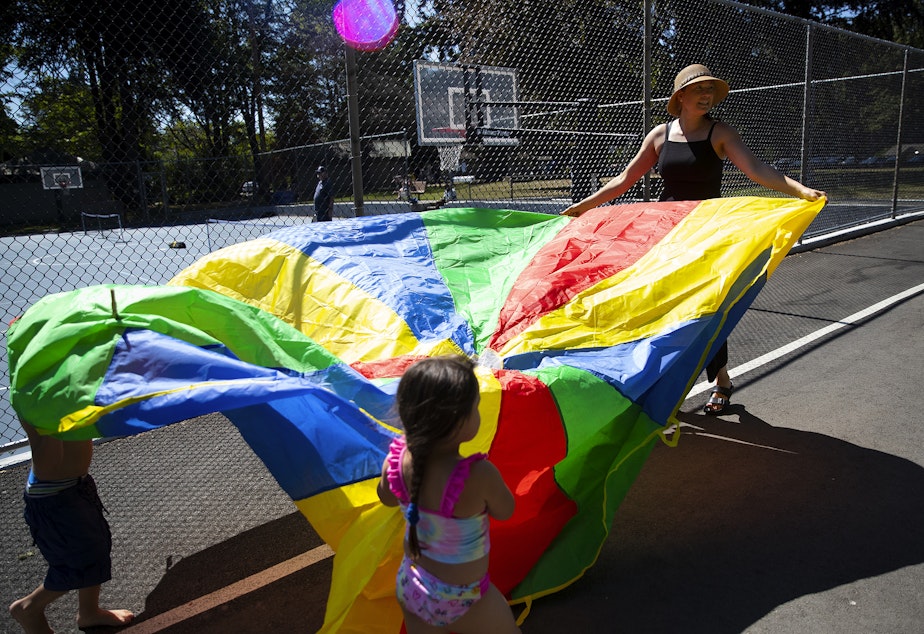 caption: Toni Gardner, lead case manager with Sound Pathways, right, helps Vay, 5, to carry a rainbow parachute while playing on Wednesday, August 17, 2022, at a park.