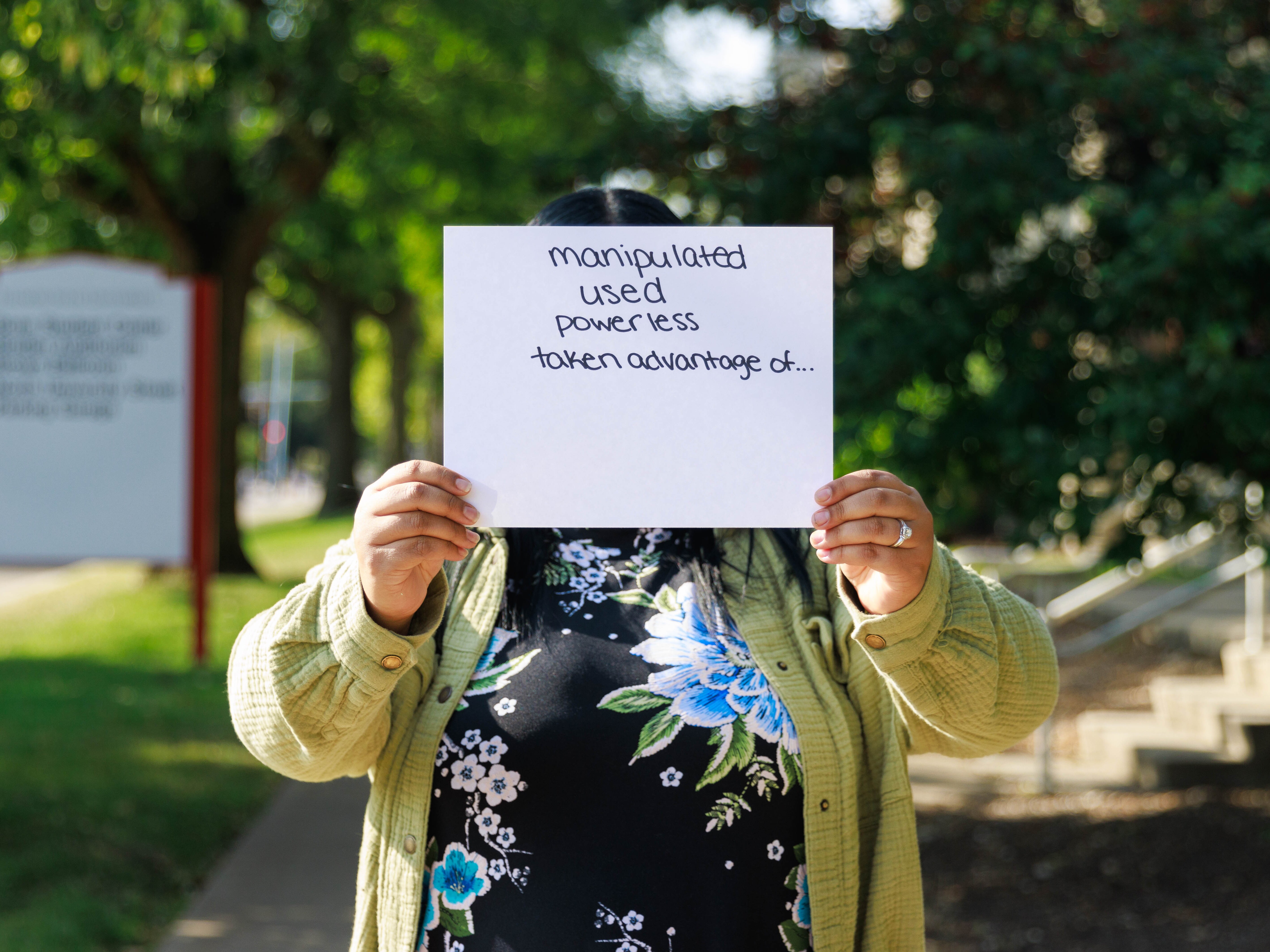 caption: Daisy is a former crisis counselor at the local 988 call center in Bloomington, Ill. She holds a paper in front of her face listing emotions she felt when taking abusive calls while working there. She covers her face to maintain anonymity because she doesn’t want her personal or professional networks to know about the abuse. Daisy is the name she used with callers during her work shifts.