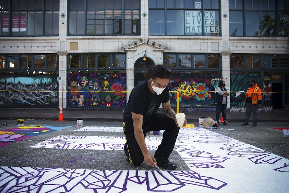 caption: Mixed media artist Future Crystals paints the letter E in the Black Lives Matter street mural on Friday, October 2, 2020, on E. Pine Street in Seattle. 