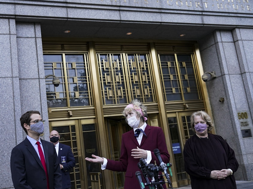 caption: E. Jean Carroll (center), who says former President Donald Trump raped her in the 1990s, speaks to reporters as she leaves the courthouse in New York following an October hearing in her defamation lawsuit. The Justice Department said Tuesday it will continue its defense of Trump.