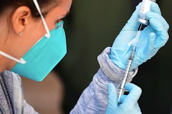 caption: A health care worker draws a dose of Moderna's COVID-19 vaccine into a syringe for an immunization event in the parking lot of the L.A. Mission on Feb. 24.