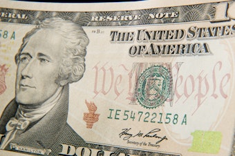caption: A close-up of the front of the US 10-dollar bill bearing the portrait of Alexander Hamilton, America's first Treasury Secretary.