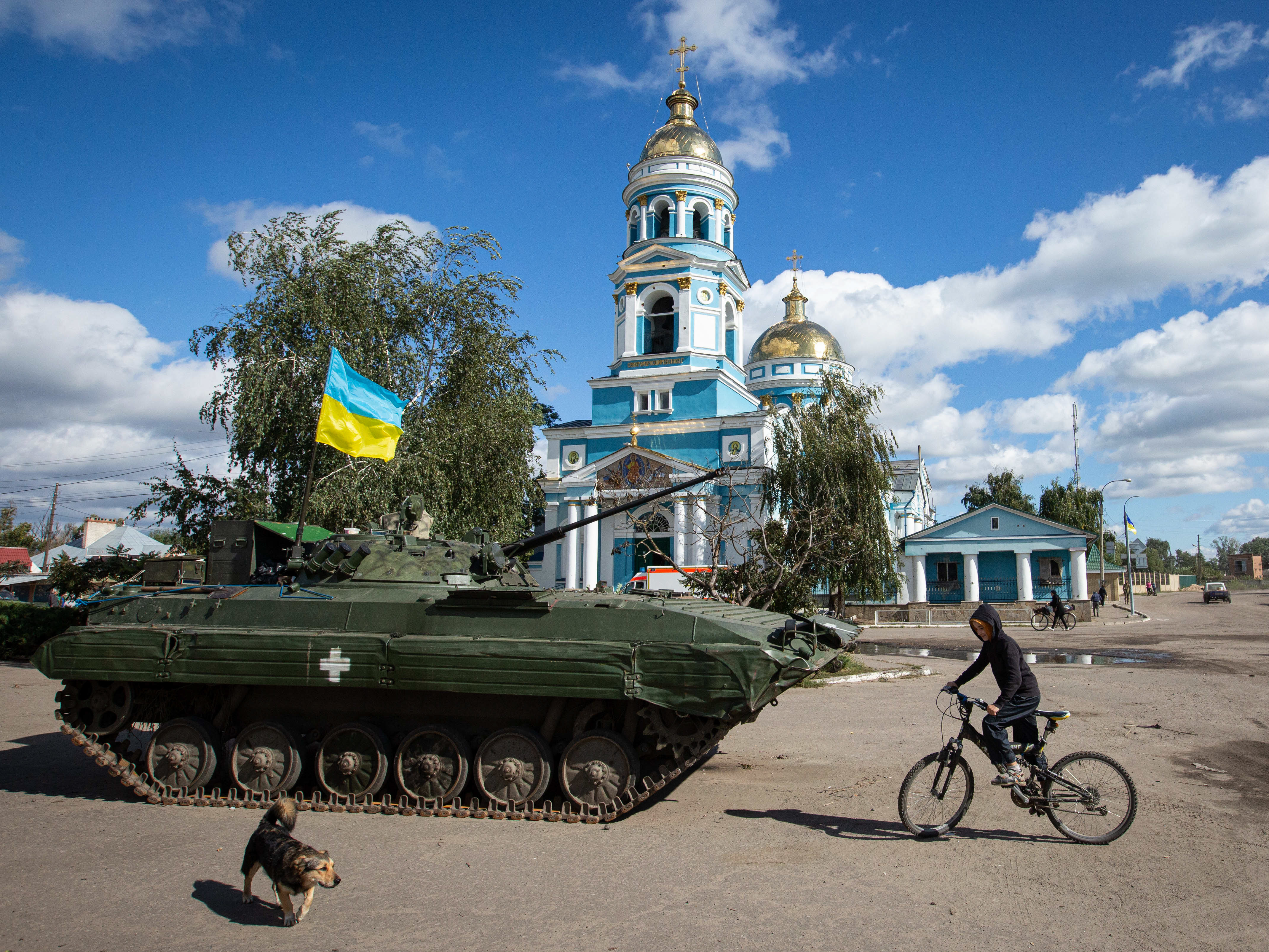caption: A boy rides a bicycle near an armored tank with a Ukrainian flag in the town of Izium, recently liberated by Ukrainian armed forces, in the Kharkiv region on Monday. Russian troops occupied Izium on April 1.