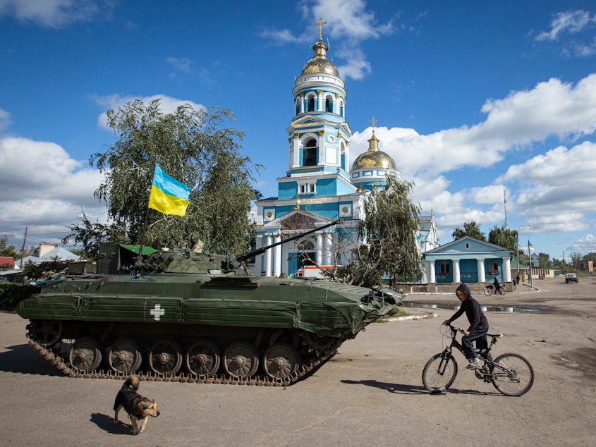 caption: A boy rides a bicycle near an armored tank with a Ukrainian flag in the town of Izium, recently liberated by Ukrainian armed forces, in the Kharkiv region on Monday. Russian troops occupied Izium on April 1.