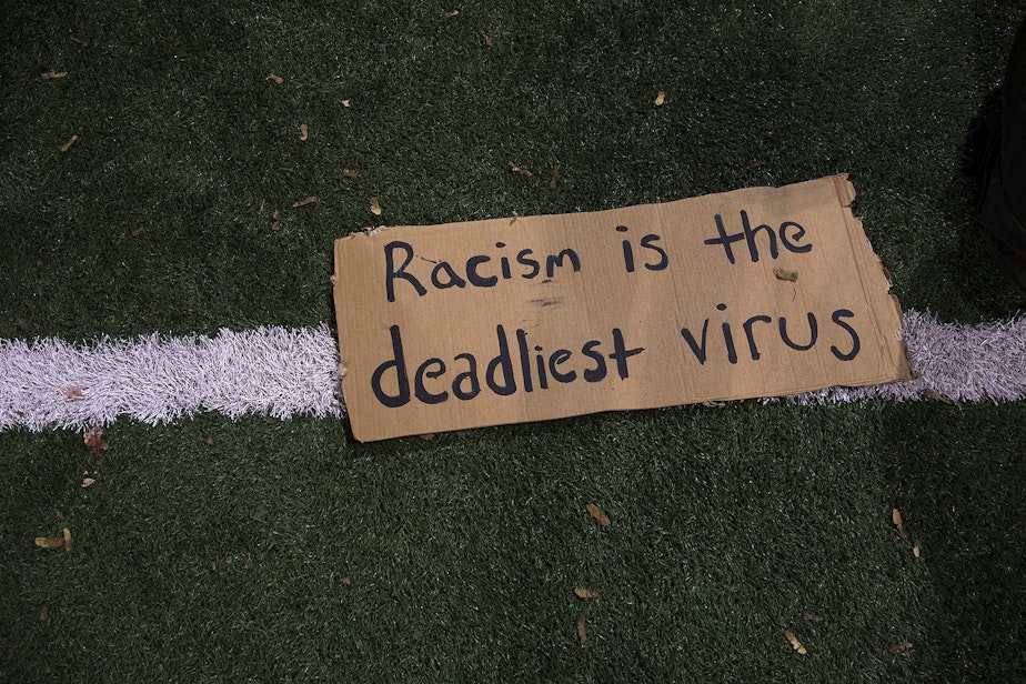 caption: 'Racism is the deadliest virus' is written on a piece of cardboard on Monday, October 26, 2020, during the 150th day of protests for racial justice in Seattle, at Cal Anderson Park.