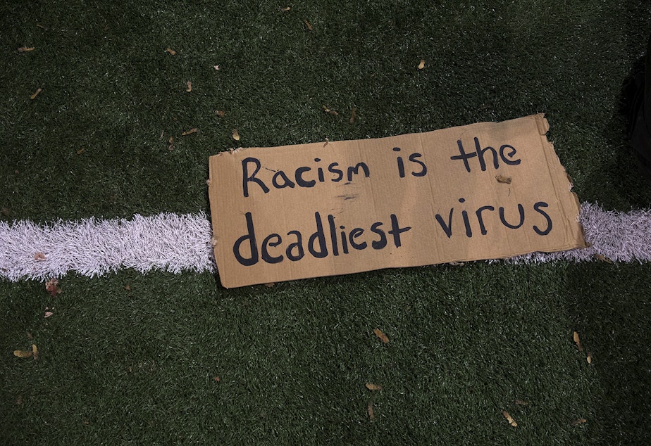 caption: 'Racism is the deadliest virus' is written on a piece of cardboard on Monday, October 26, 2020, during the 150th day of protests for racial justice in Seattle, at Cal Anderson Park.
