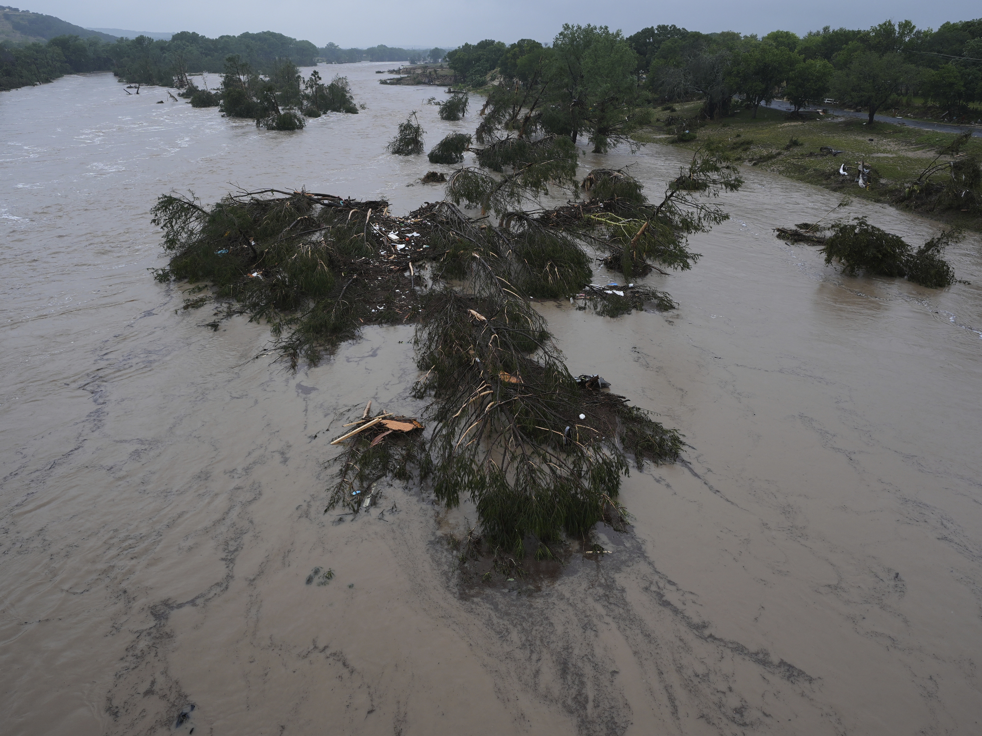caption: A raging Guadalupe River leaves fallen trees and debris in its wake in Kerrville, Texas.