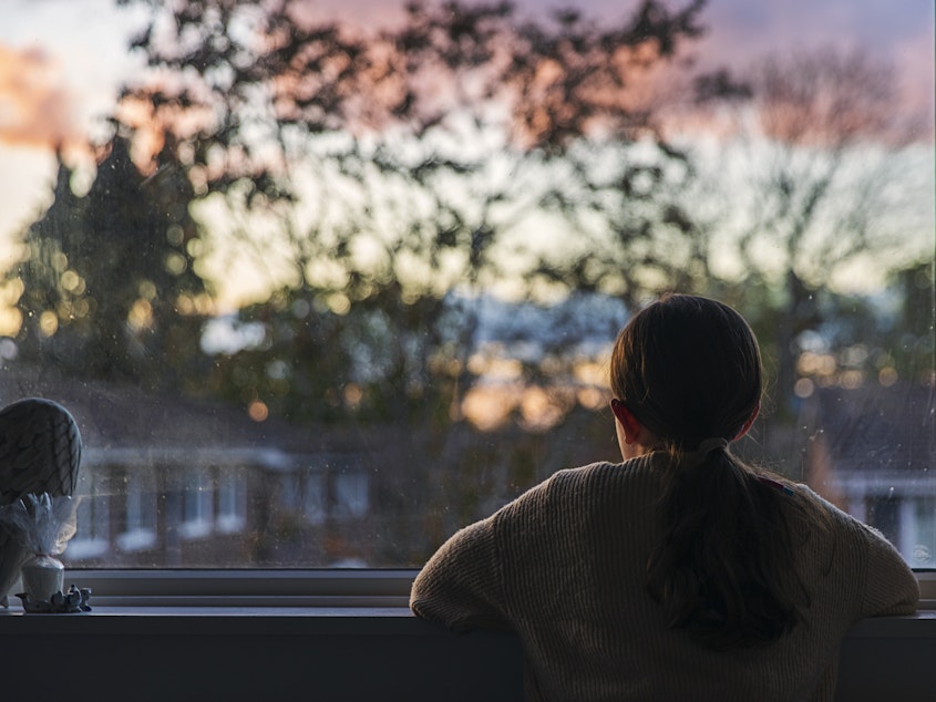 caption: A young girl looks out of her bedroom window as the sun is setting.