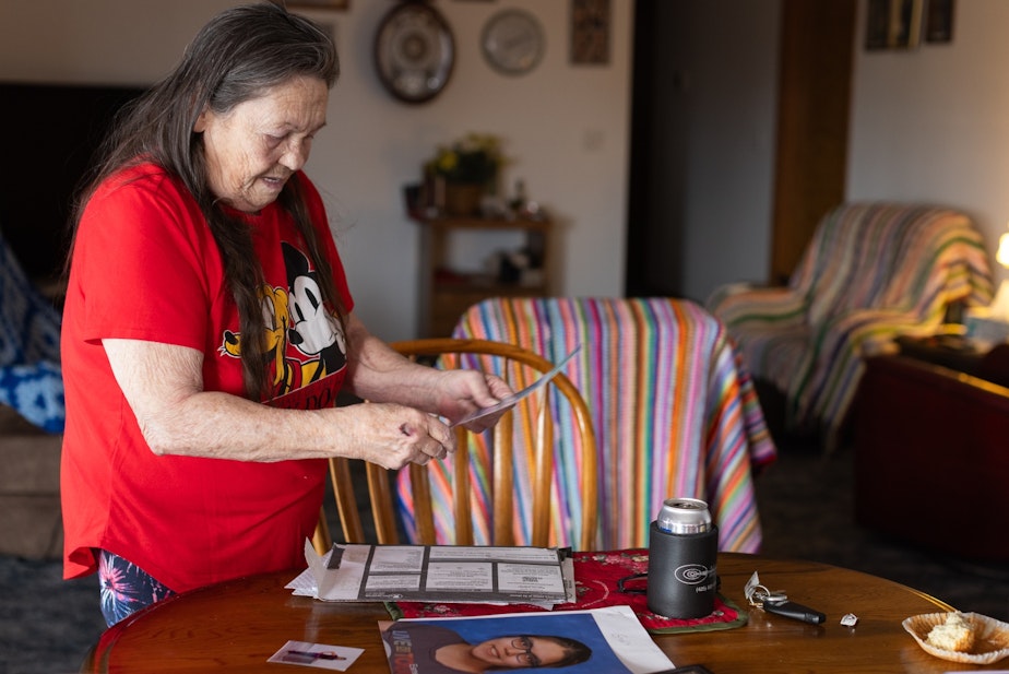 caption: Bonnie Groo looks through portraits of her great-grandchild, Kit Nelson-Mora, in her home in Yakima, Wash., in November 2023. Bonnie, who raised Kit along with her former husband, hasn’t heard from Kit in over two years.