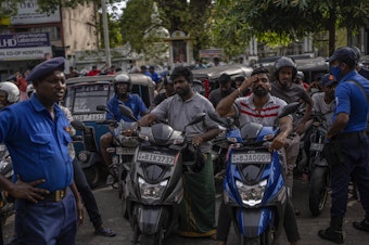 caption: Police officers stand guard as people wait in queue to buy petrol at a fuel station, in Colombo, Sri Lanka, July 17, 2022.
