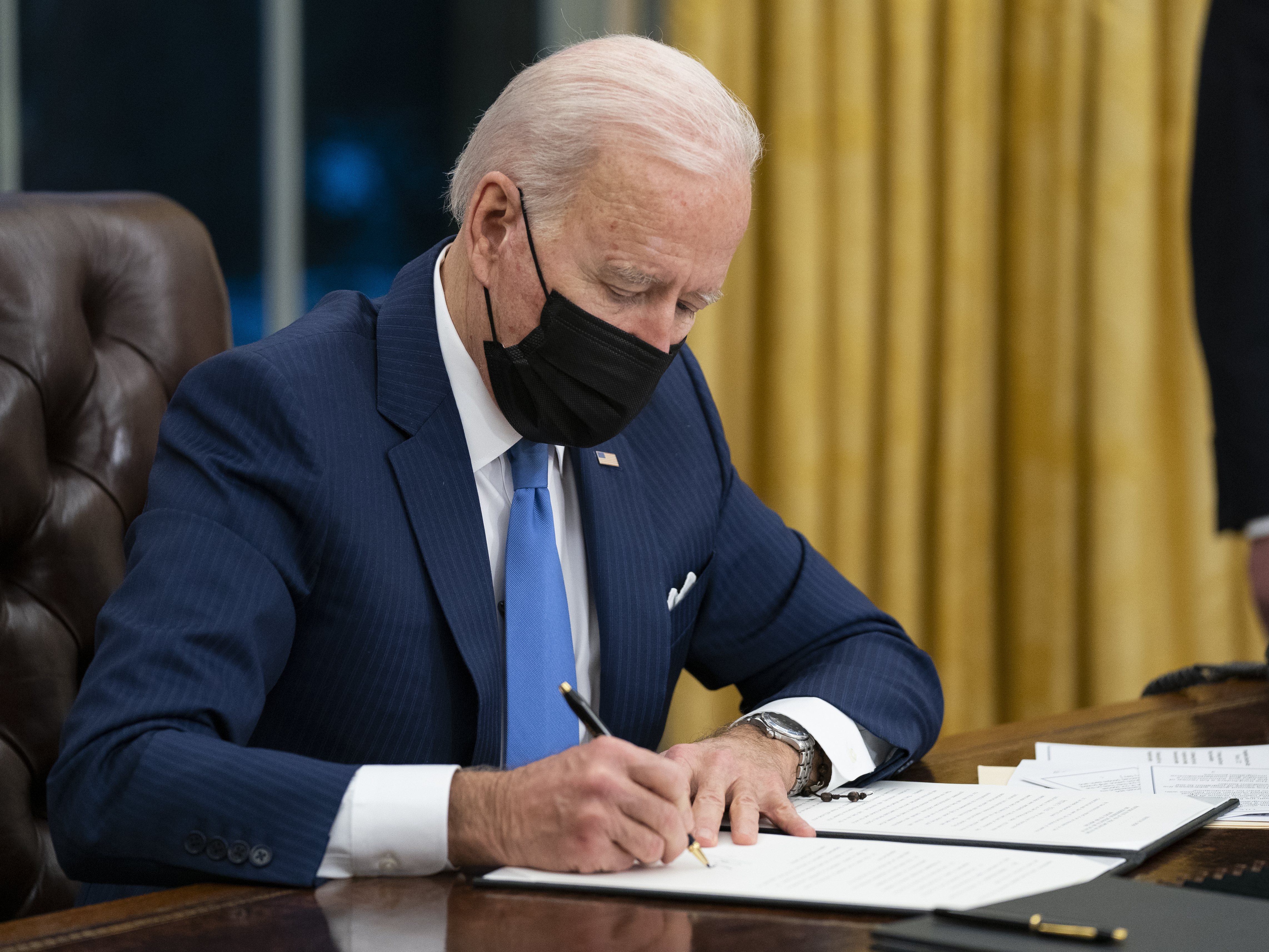 caption: President Biden signs an executive order on immigration in February in the Oval Office.